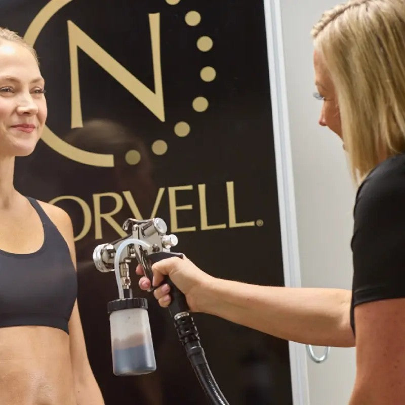 Spray tan artist salary blog image featuring local business owner Marcy spray tanning a client