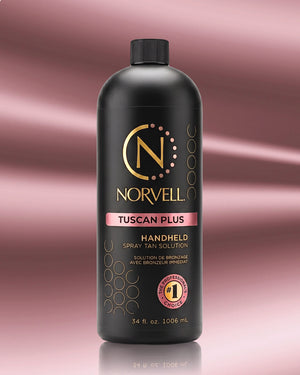 A bottle of Norvell Tuscan Plus Handheld Spray Tan Solution, featuring a matte black bottle with gold and pink accents, set against a pink gradient background with a soft reflection.