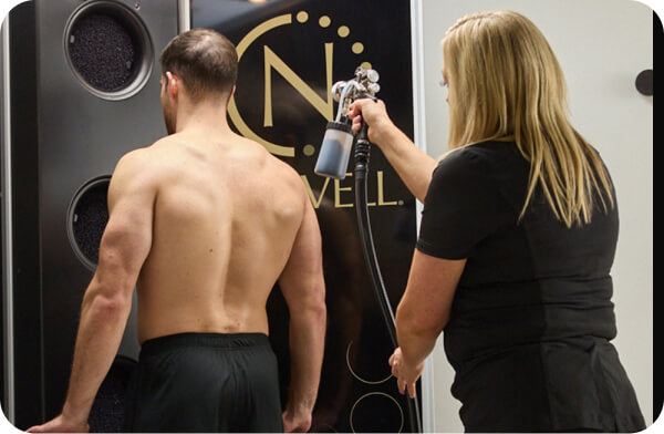 Instructor spraying male client’s back in Nashville spray tan class